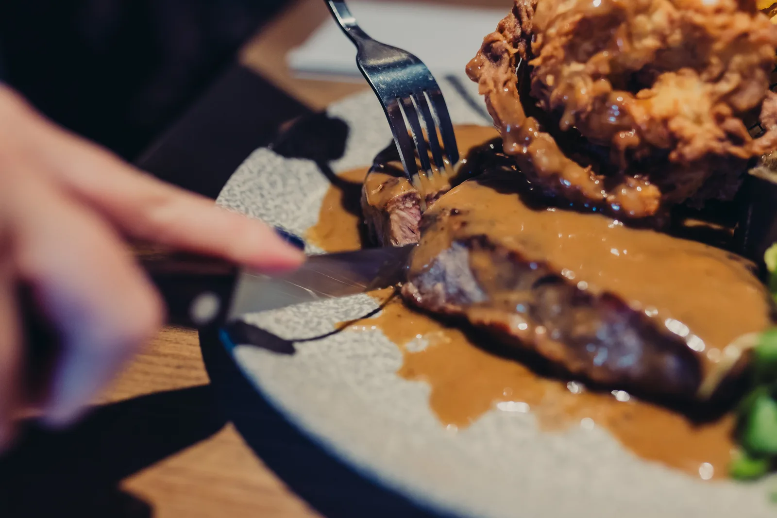 Someone cutting into Sirloin Steak with Peppercorn Sauce on it